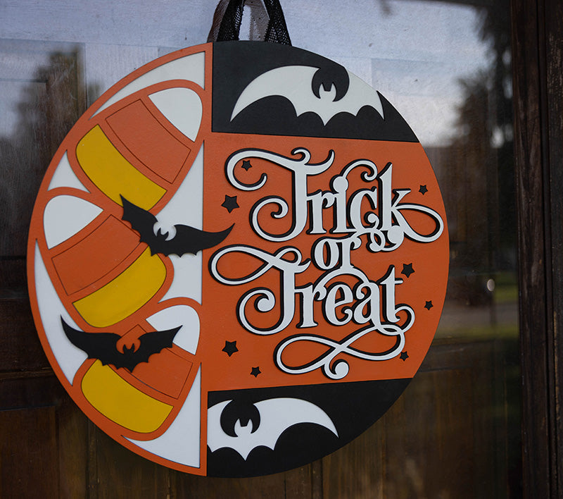 Halloween-themed decorative door hanger with candy corn, bats, and 'Treat or Trick' text on a wooden background from Thistlewood Creations.