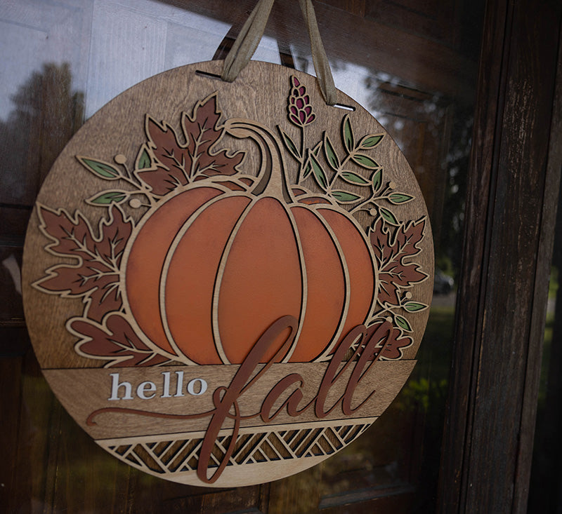 Wooden circular  door hanger with pumpkin and leaves design, featuring 'hello fall' text from Thistlewood Creations.