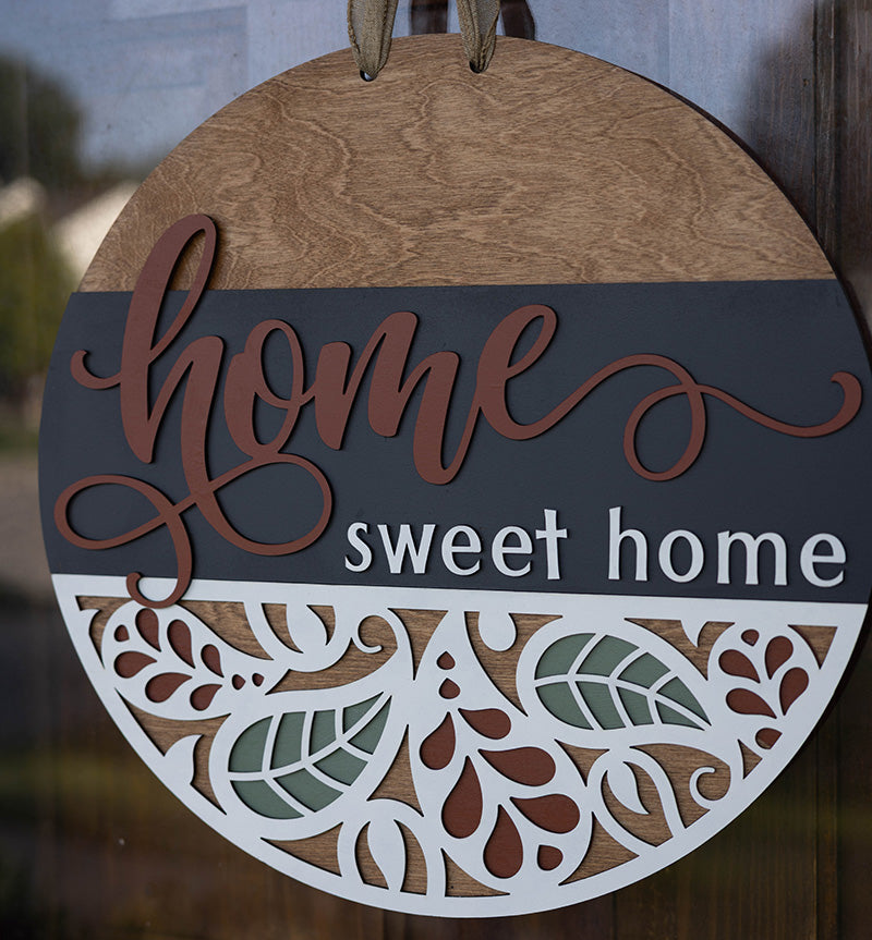 Decorative door hanger with 'home sweet home' text and paisley leaf patterns on a wooden background from Thistlewood Creations
